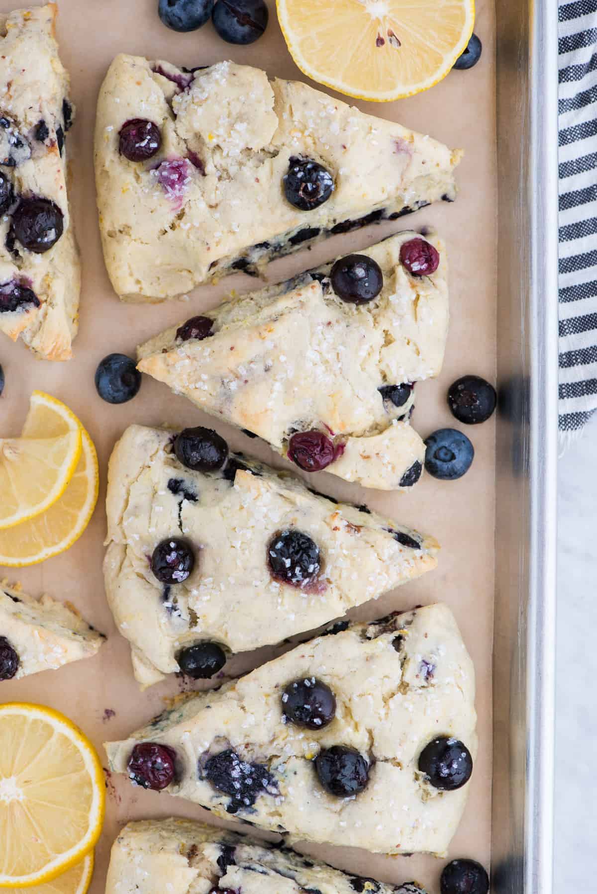lemon blueberry scones on brown parchment paper with lemon slices and blueberries