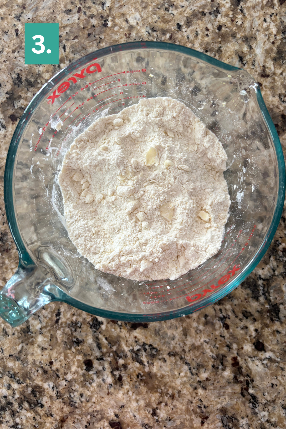 A glass Pyrex measuring cup filled with flour and small clumps of butter sits on a granite countertop, ready for baking delicious lemon blueberry scones. A green box labeled 3. is in the top left corner of the image.