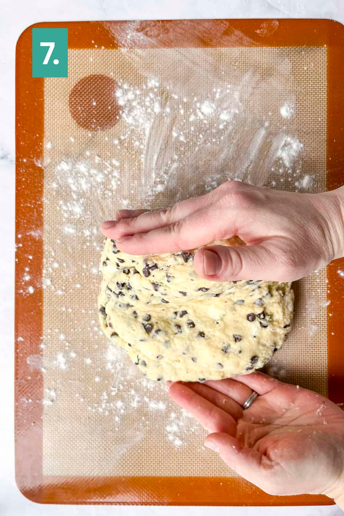 Hands forming chocolate chip scone dough on a floured silicone baking mat, with step 7 of a lemon blueberry scones recipe shown in the top left corner.