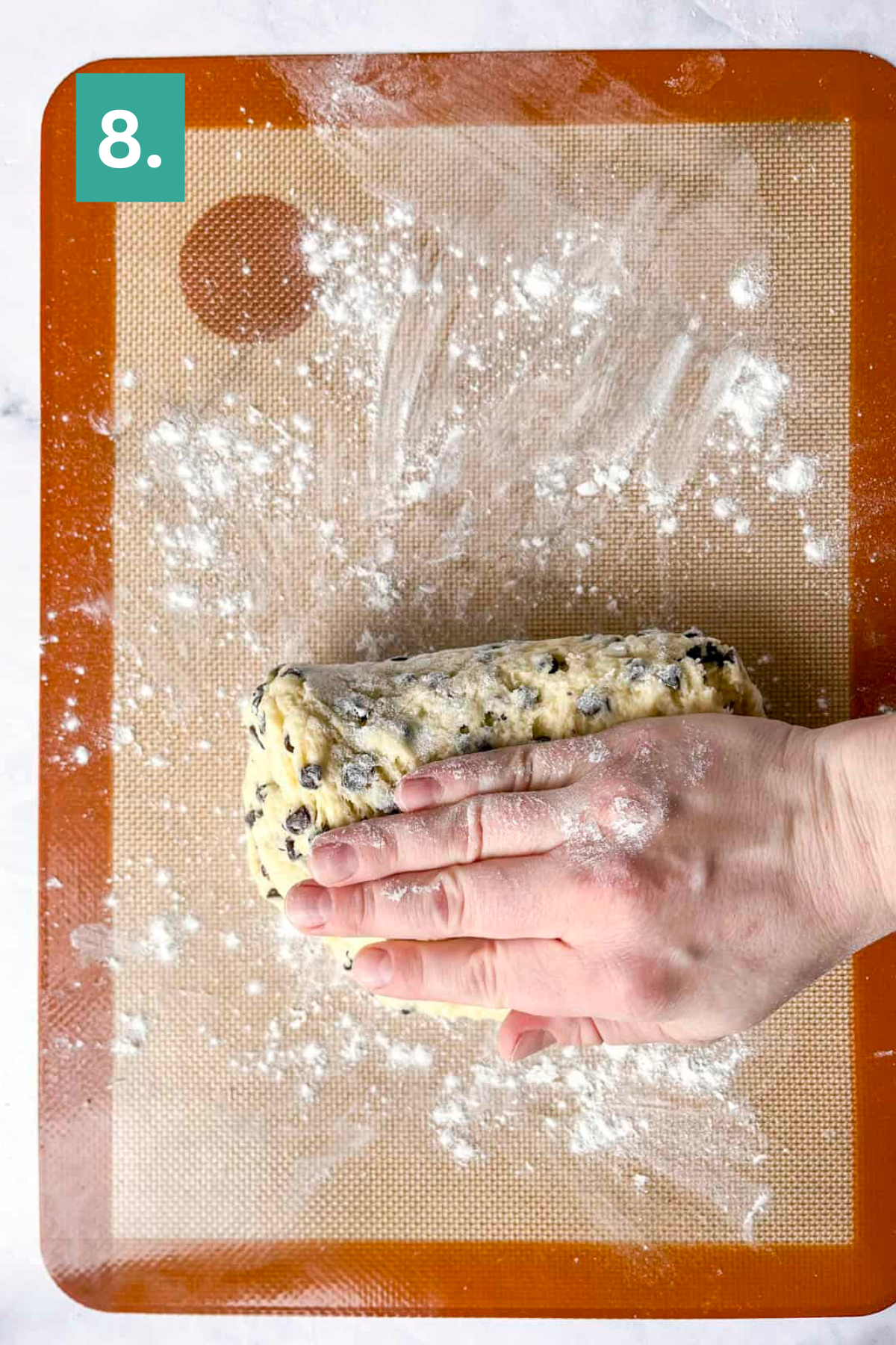 A hand shapes chocolate chip dough on a floured silicone baking mat, similar to preparing lemon blueberry scones. A green box with the number 8 appears in the top left corner, indicating this is step 8 in a recipe.