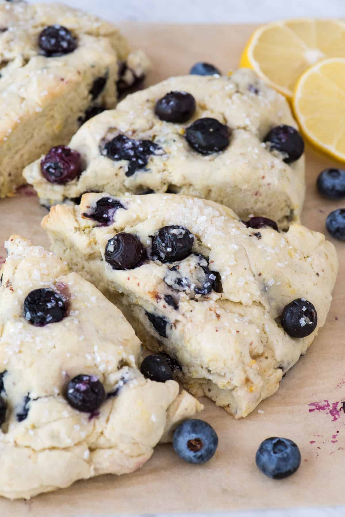 lemon blueberry scones on brown parchment paper with lemon slices and blueberries