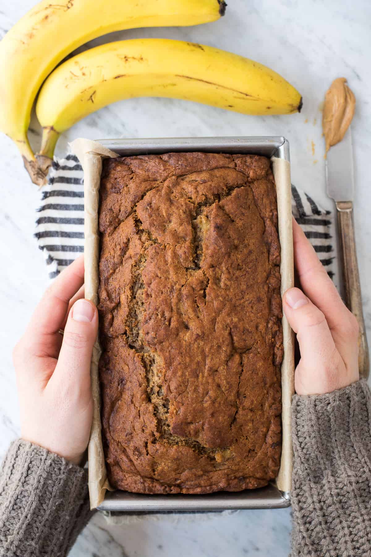 hands holding peanut butter banana bread in metal loaf pan
