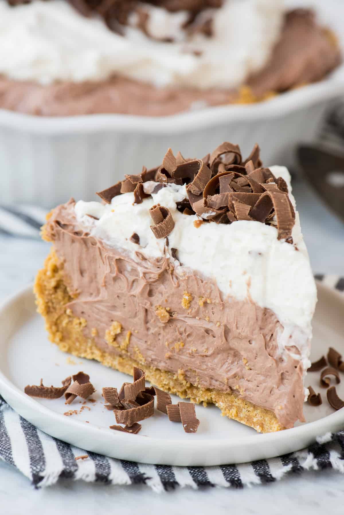 slice of chocolate pudding pie with chocolate shavings on white plate on white background