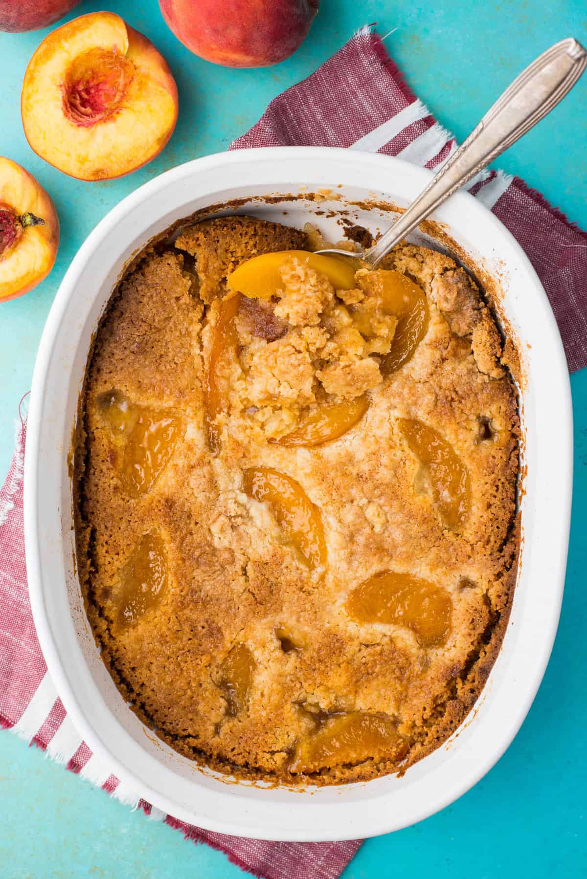 peach dump cake with spoon in white pan on teal background