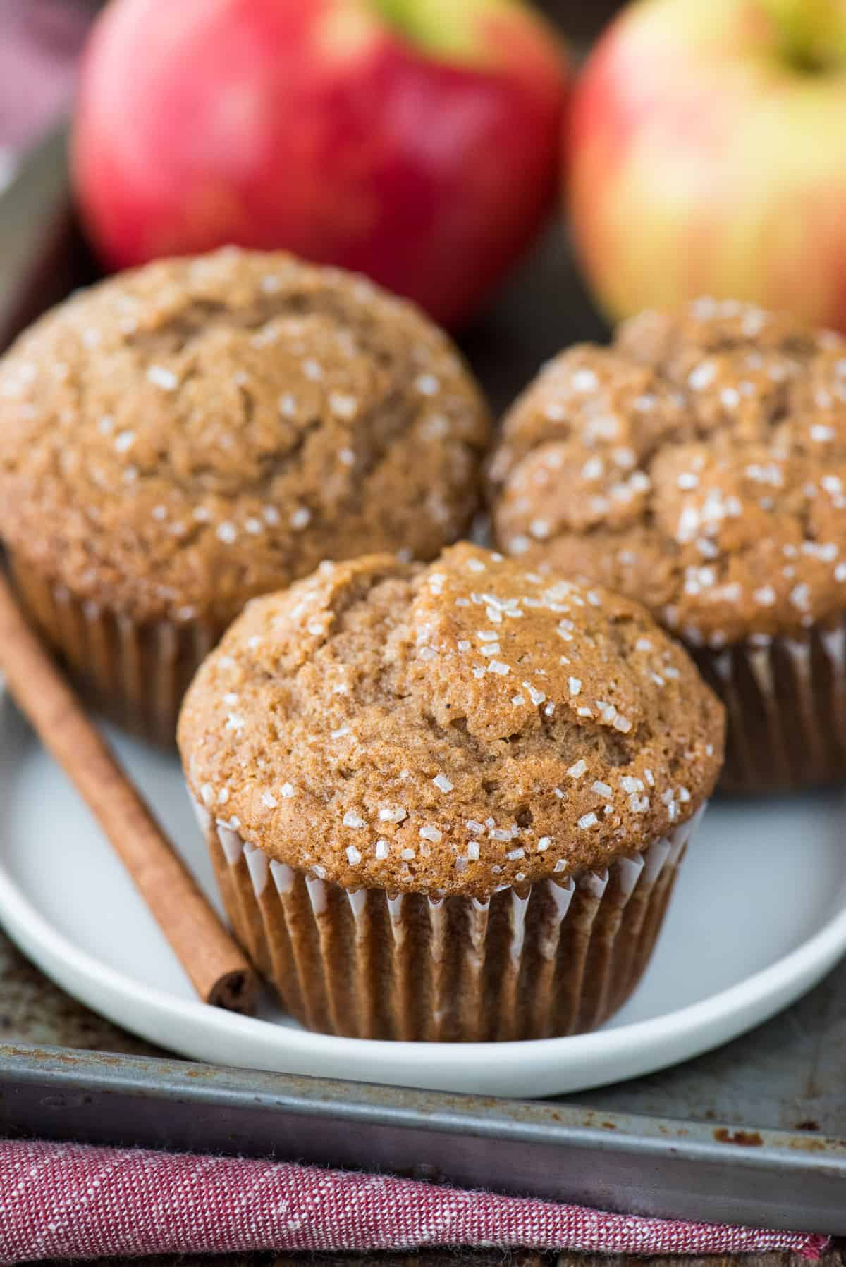 three apple muffins on white plate with cinnamon stick
