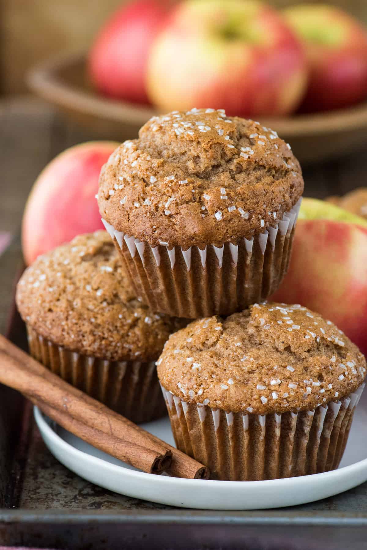 three applesauce muffins in a stack on a white plate with apples in background