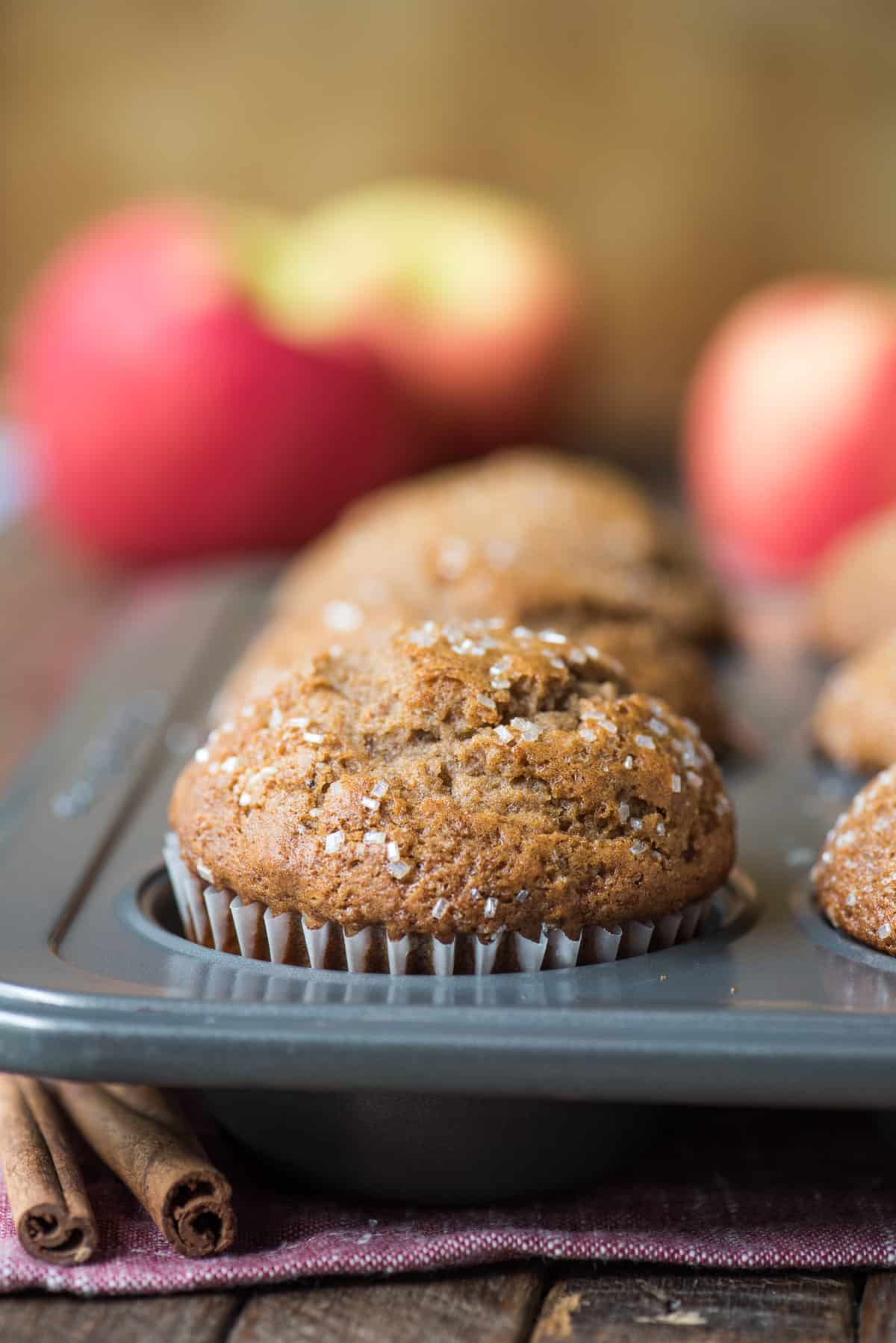 applesauce muffins in metal muffin pan with apples in background