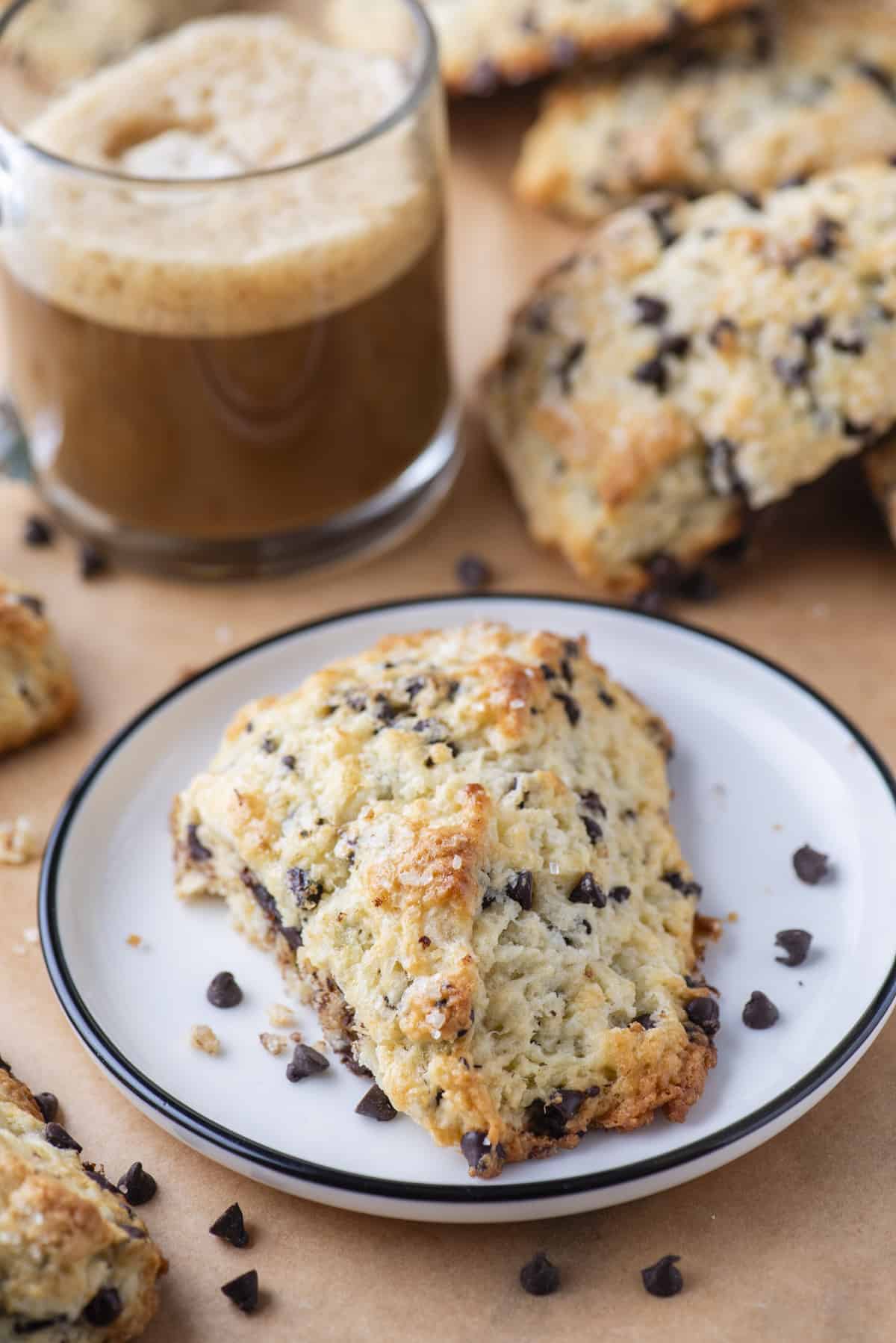 chocolate chip scones on white plate with more scones and coffee in the background