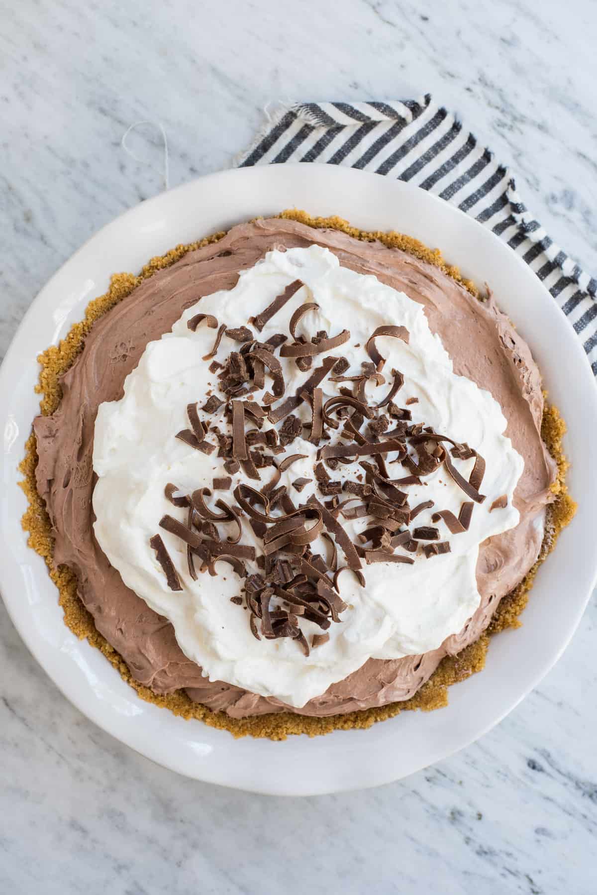 chocolate pudding pie in pie plate with graham cracker crust, whipped cream topping and chocolate shavings