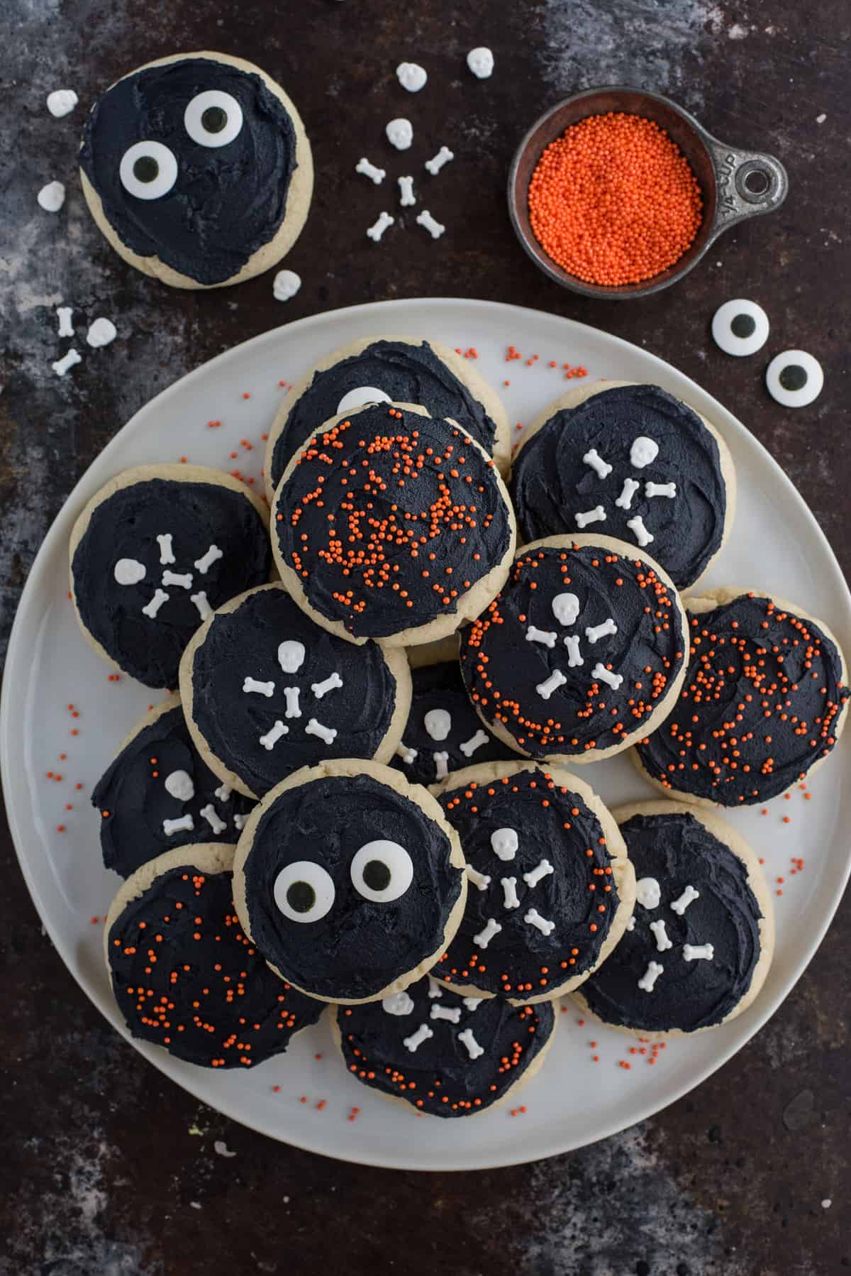 halloween sugar cookies with black frosting and various sprinkles on white plate on black background