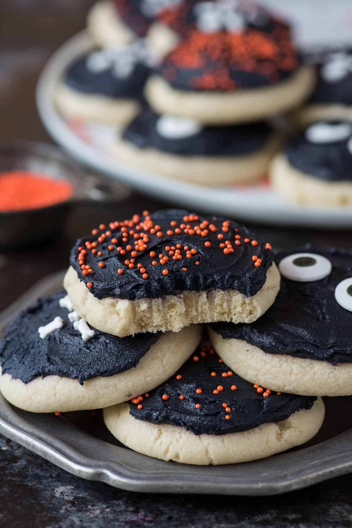 halloween sugar cookies stacked on a metal plate with bite removed from top cookie