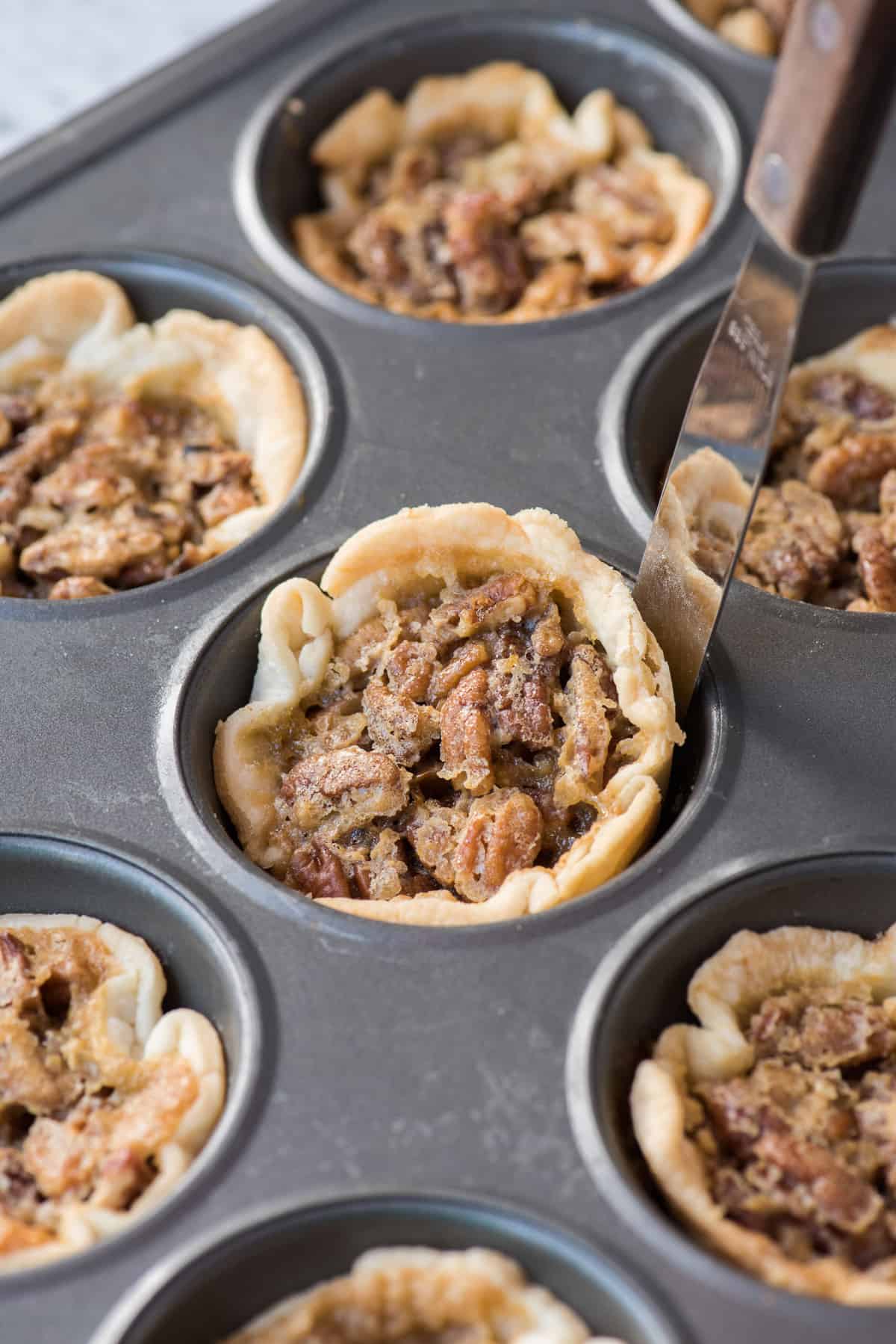 mini pecan pie in metal muffin pan being removed with metal spatula