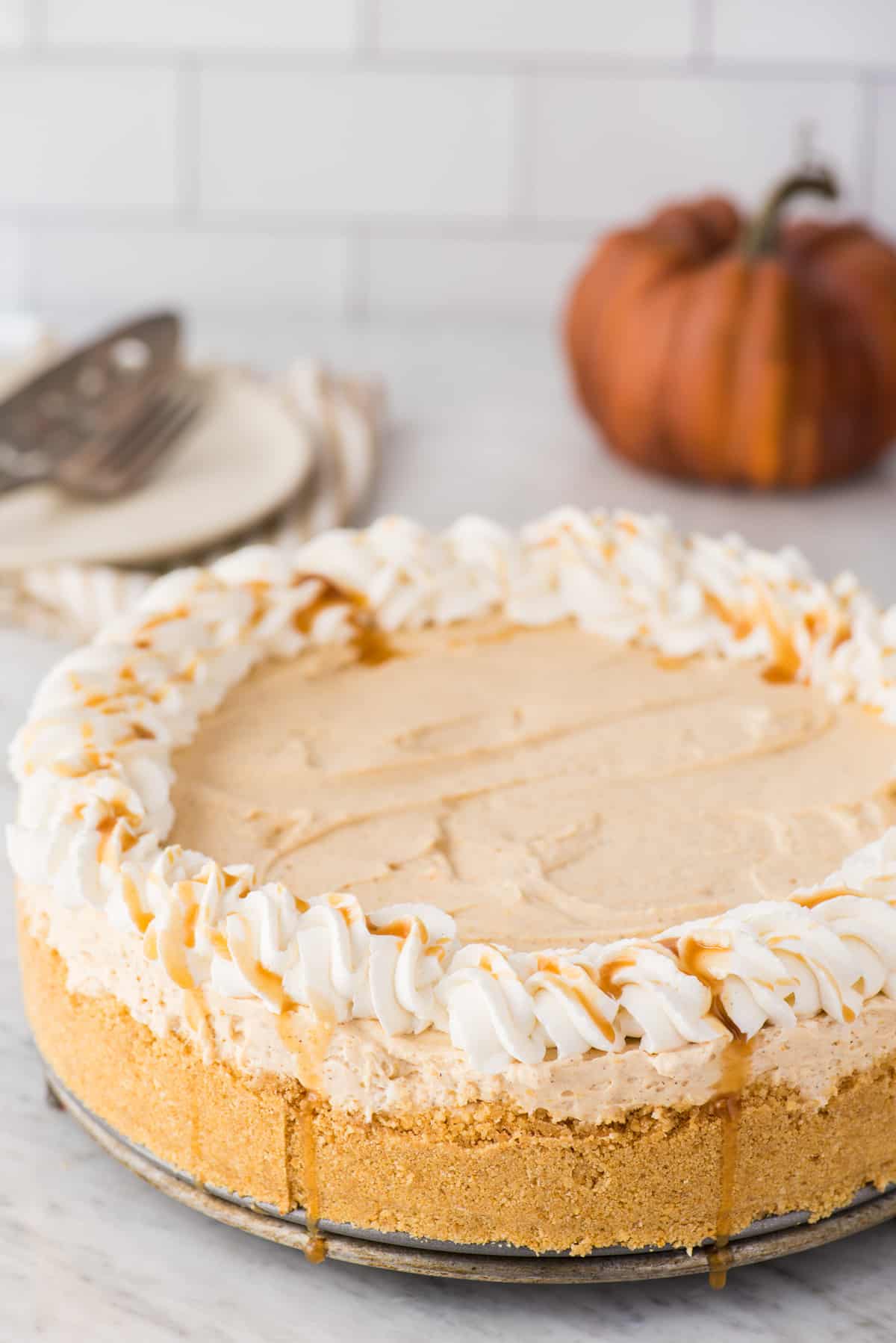 a whole pumpkin cheesecake with whipped cream and caramel drizzle around the outside on white background