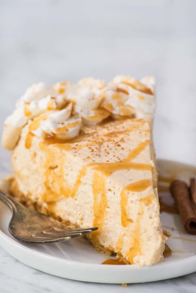 fetta di cheesecake alla zucca senza cottura con un filo di caramello in cima su piatto bianco su sfondo bianco