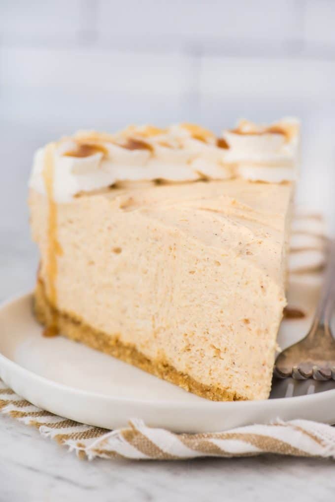 une tranche de gâteau au fromage au potiron sans cuisson sur assiette blanche avec du linge rayé sous l'assiette sur fond blanc