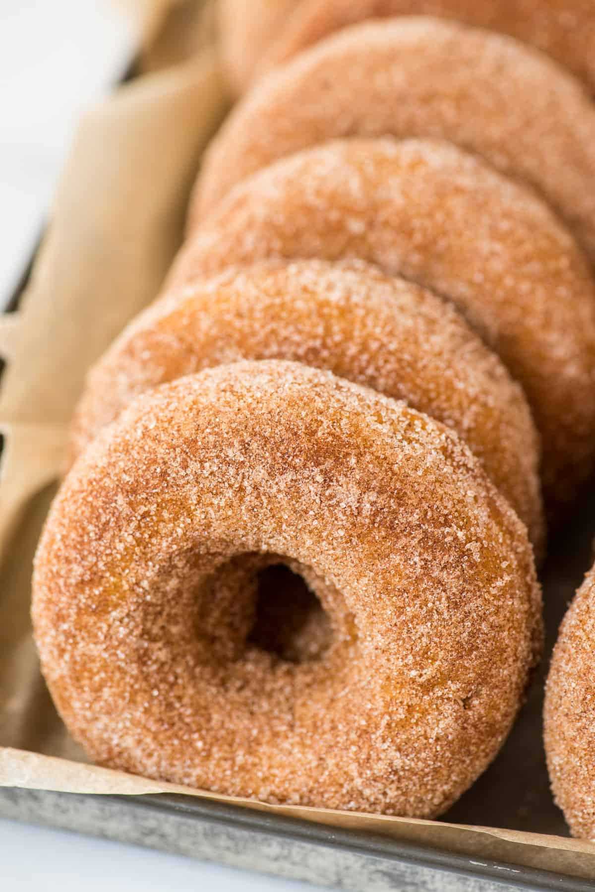 pumpkin donuts lined up in metal pan with brown parchment paper