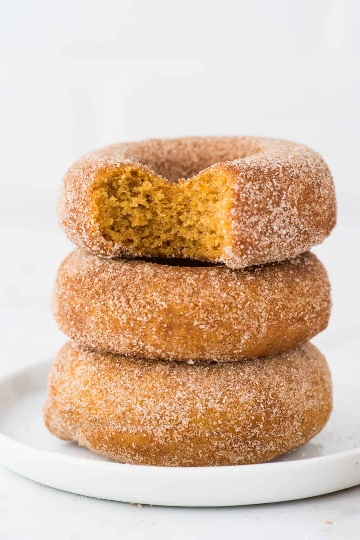 3 pumpkin spice donuts stacked on a white plate