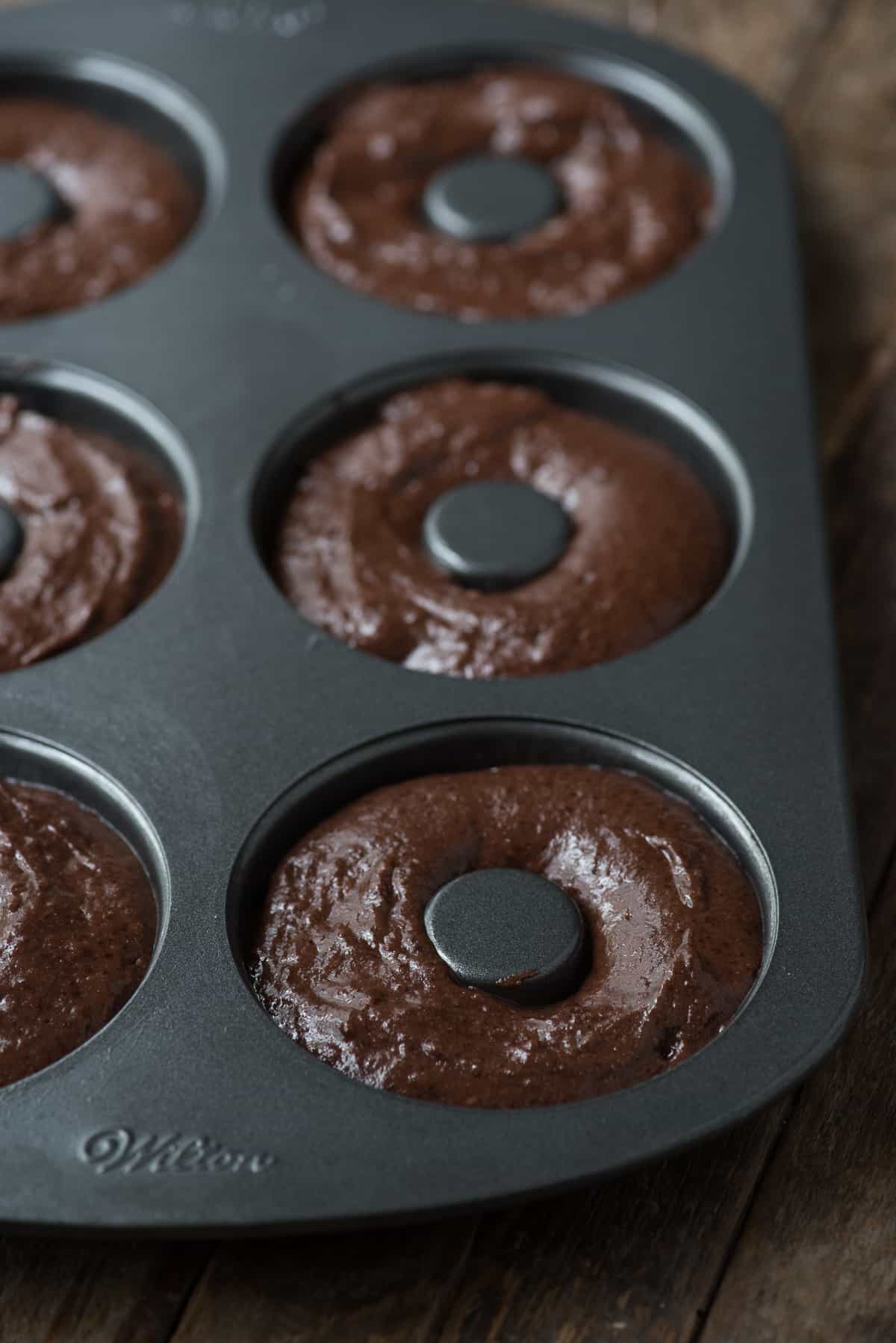 chocolate donut batter piped into metal donut pan