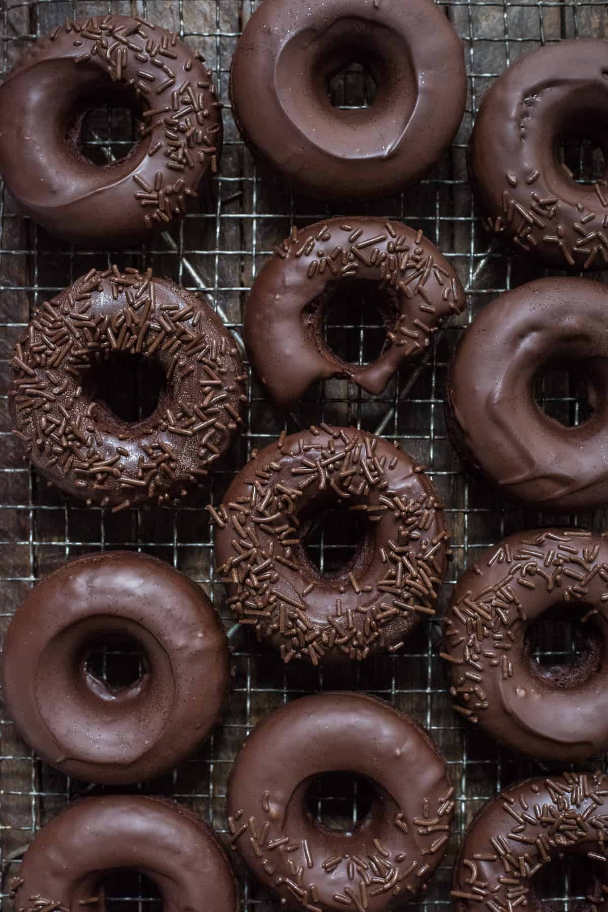 chocolate donuts with chocolate frosting in a line on metal cooling rack on dark background