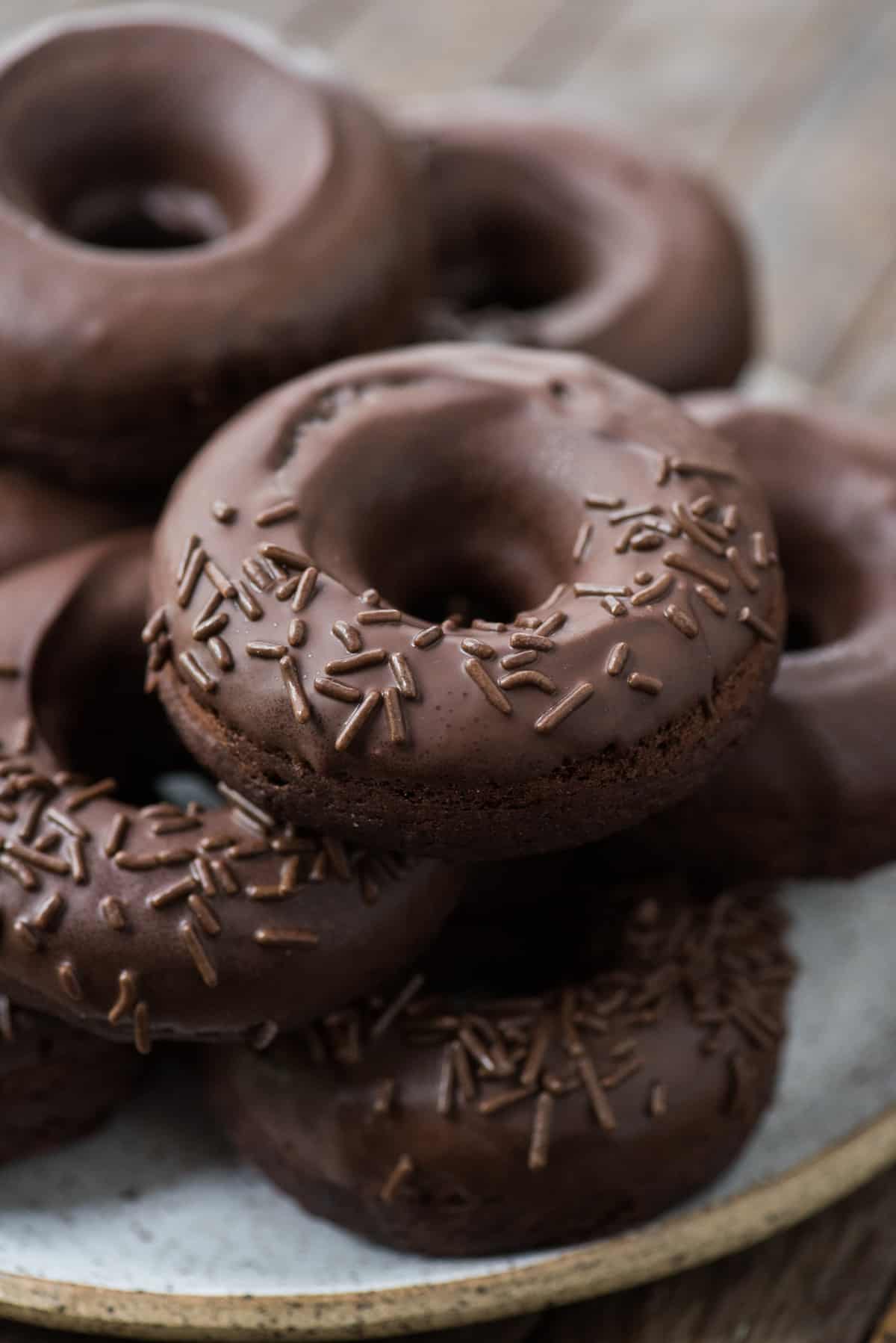 chocolate donuts with chocolate frosting and chocolate sprinkles in a stack on white plate
