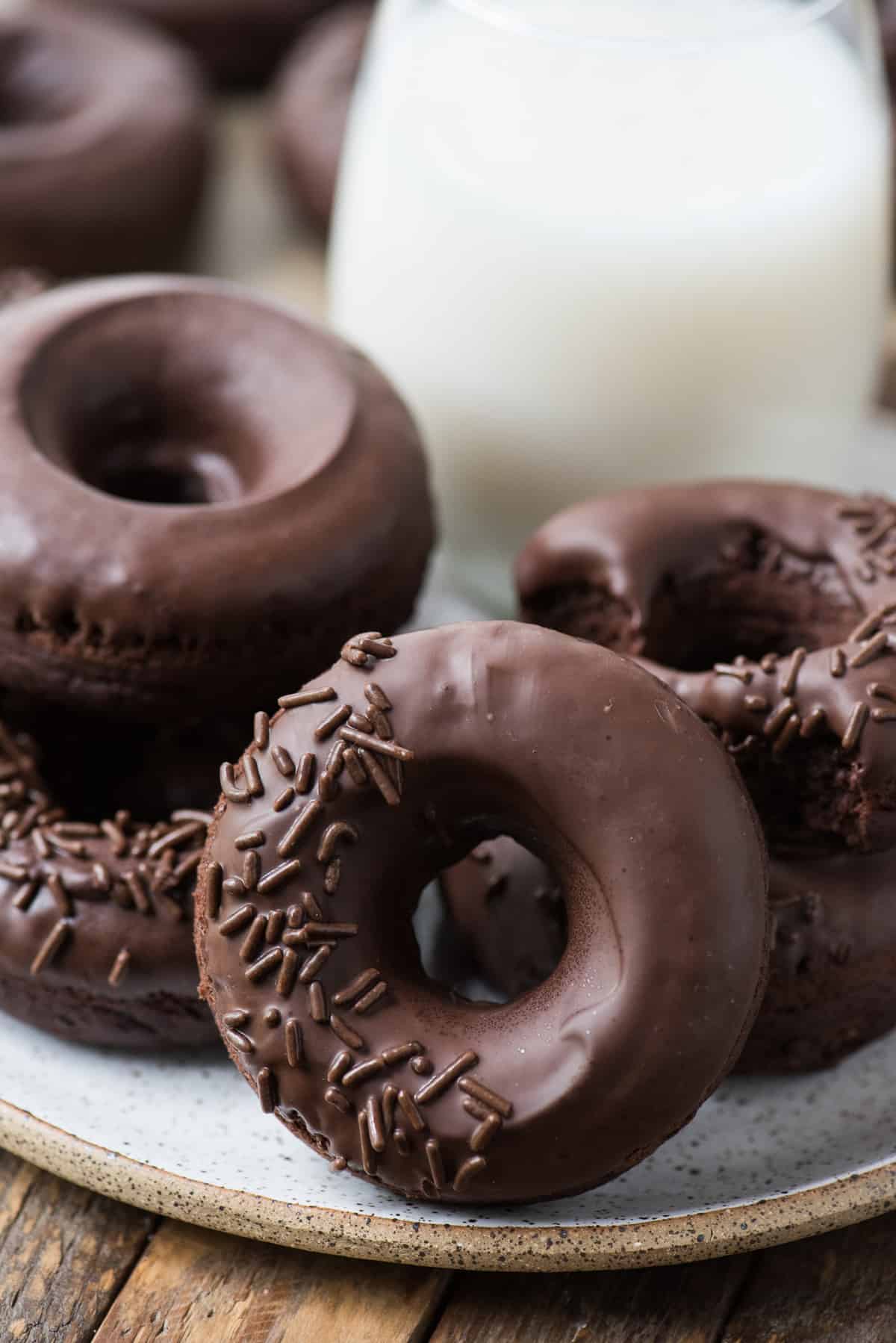 chocolate donuts with chocolate frosting on white plate with glass of milk in the background