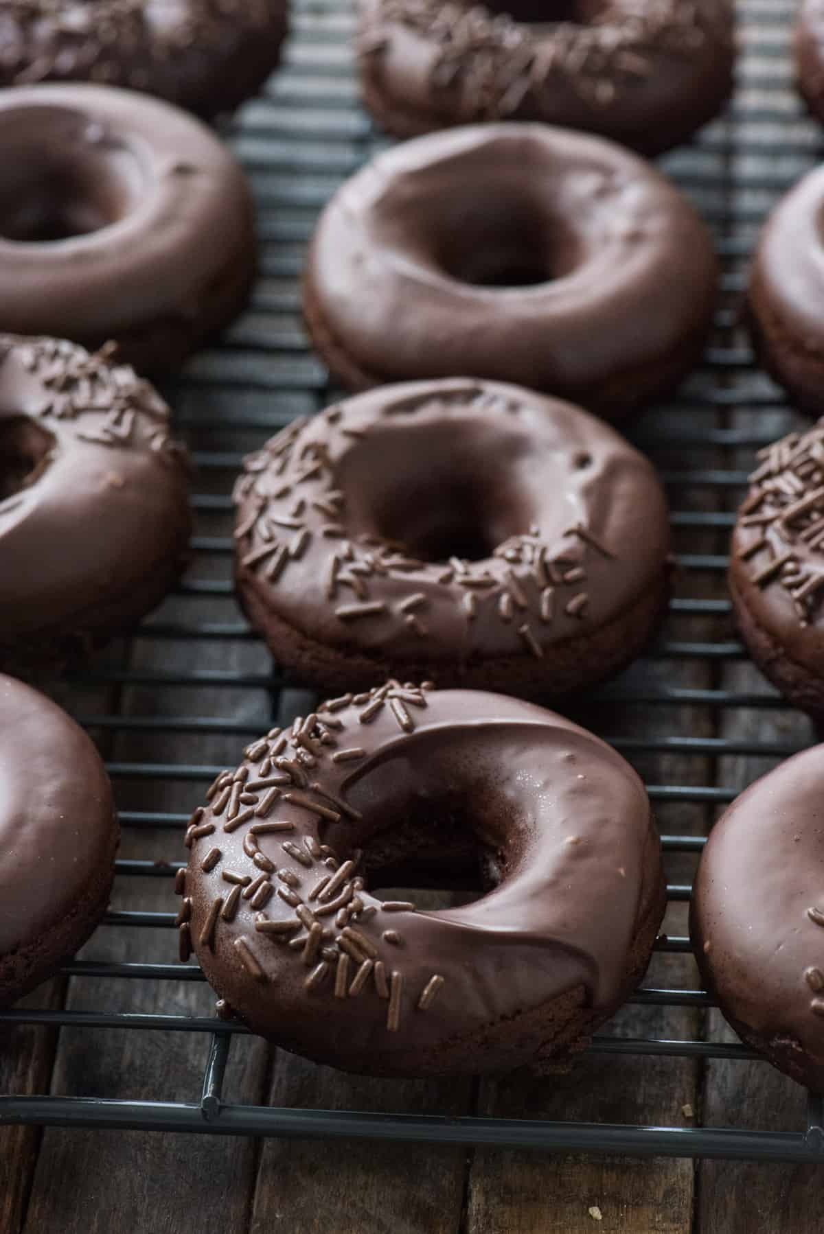 chocolate donuts with chocolate frosting in a line on metal cooling rack on dark background