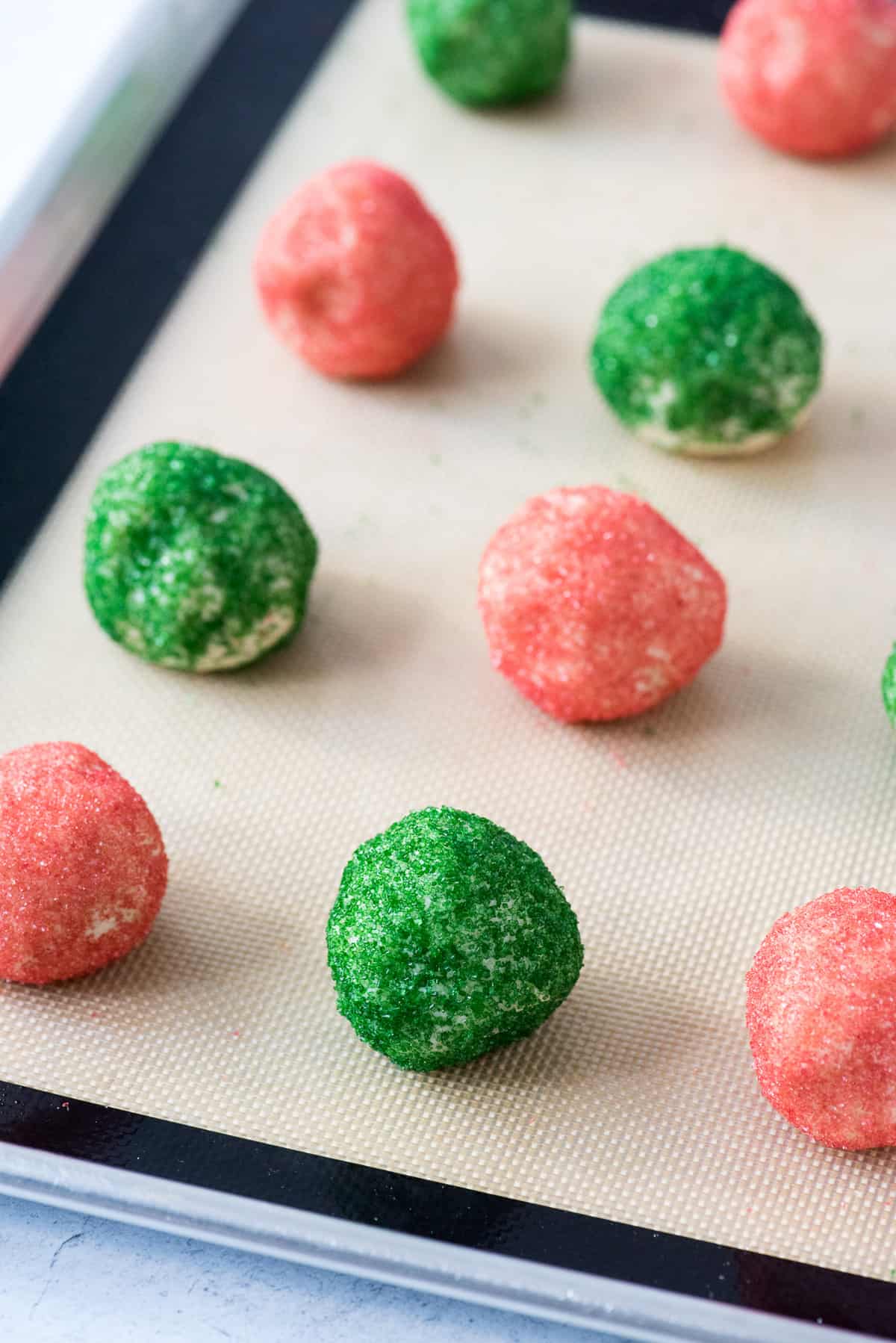red and green cookie dough balls on baking sheet lined with silicone mat