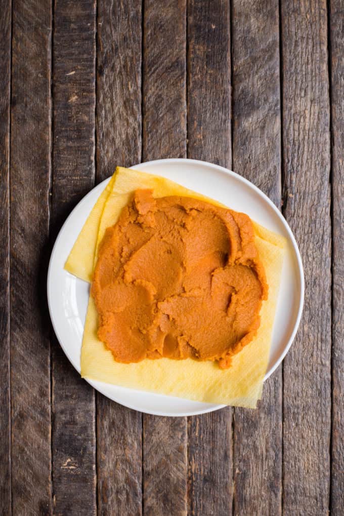 A white plate on a wooden surface holds a yellow cloth with an orange-brown paste spread on top, reminiscent of the rich hues found in pumpkin sugar cookies.