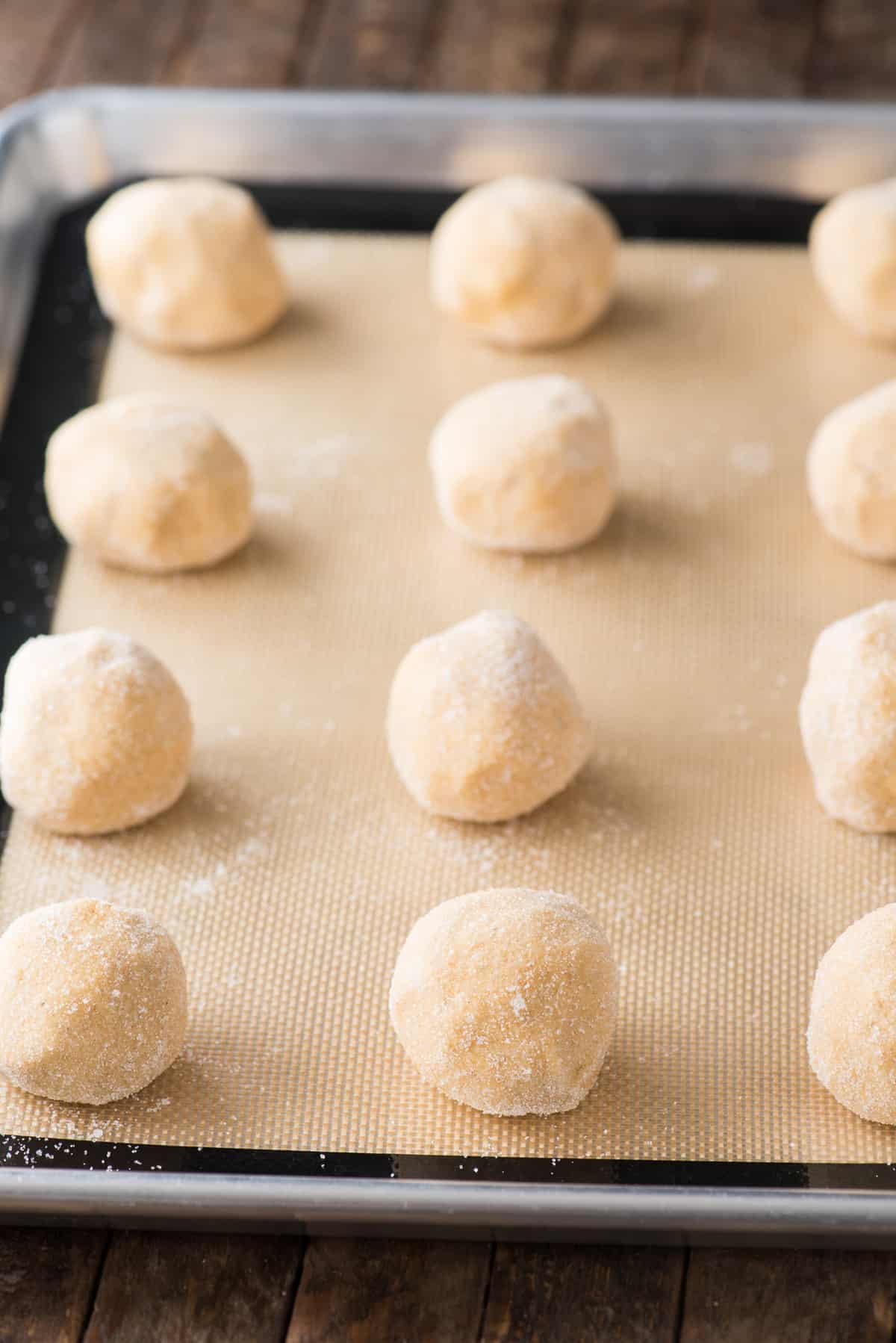 pumpkin cookie dough balls rolled in sugar lined up on a silicone baking mat