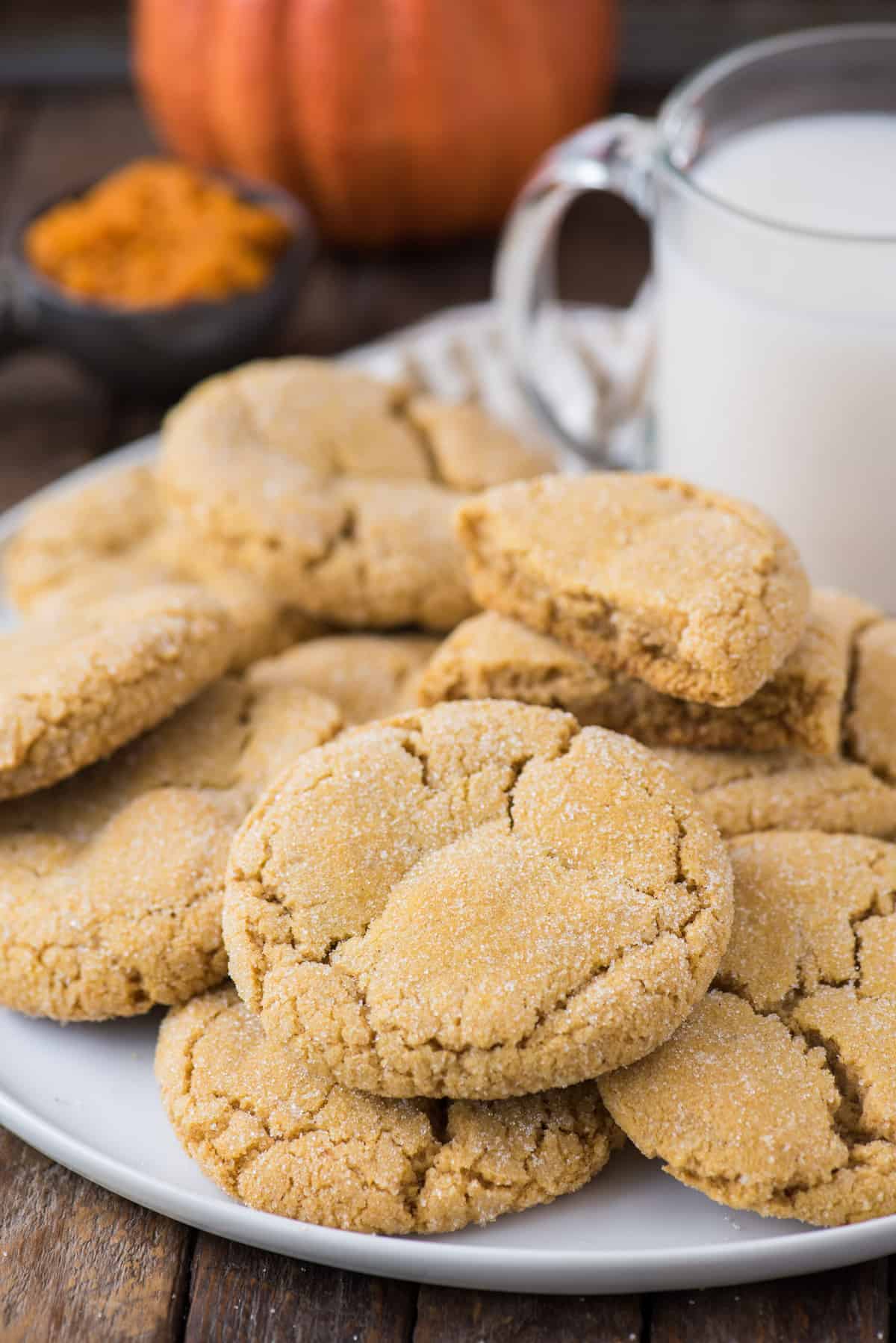 pumpkin cookies piled on white serving tray with a glass of milk and pumpkin in the background