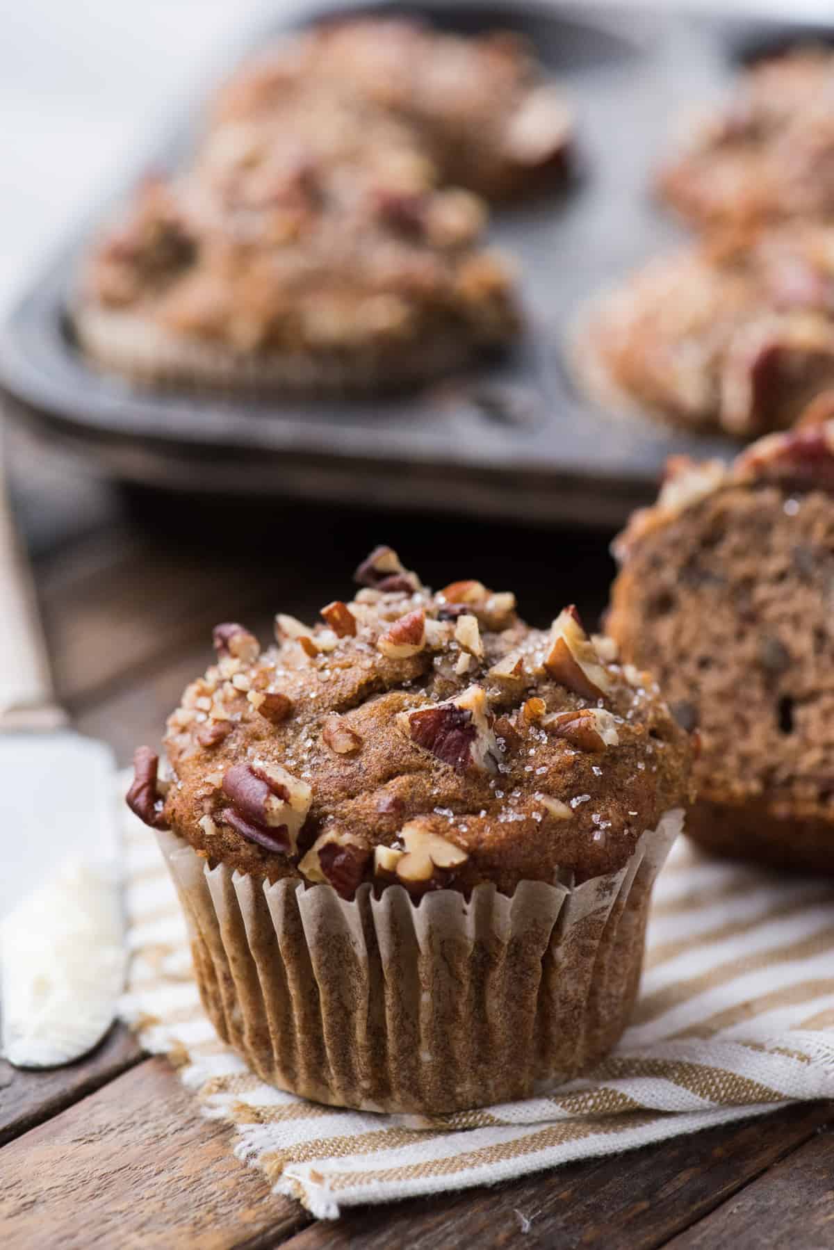 banana nut muffin on striped linen towel with muffin pan in the background on dark wood background