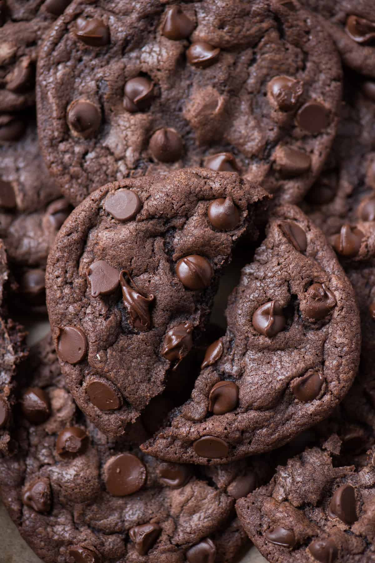 close up of one double chocolate chip cookie broken in half with gooey chocolate chips