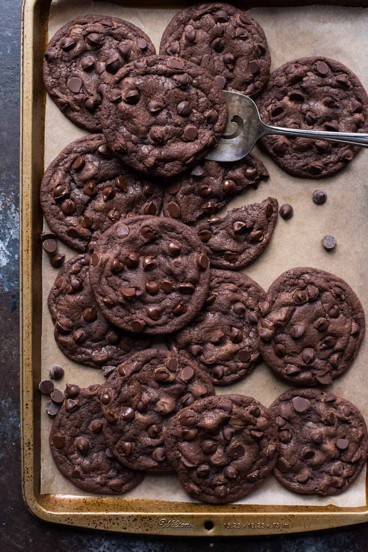 double chocolate chip cookies arranged on brown parchment paper with metal cookie spatula under one cookie