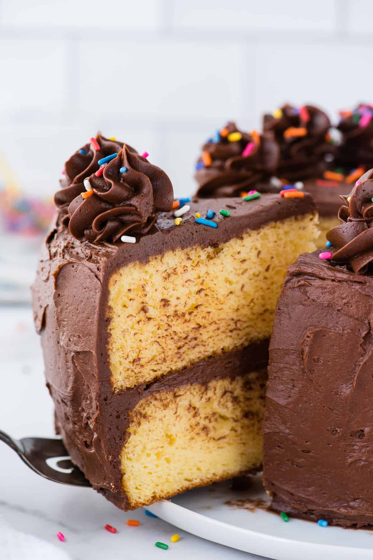 slice of yellow cake with chocolate frosting being removed from cake