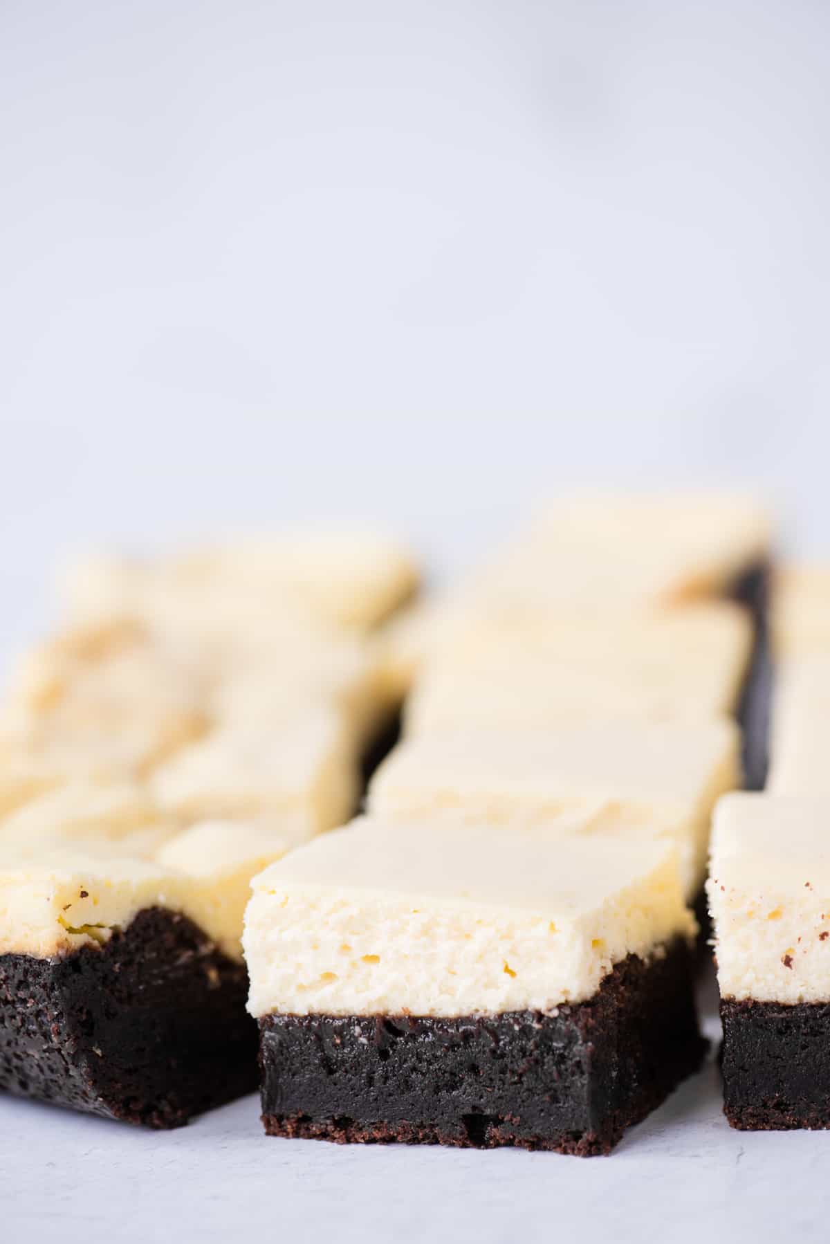 cheesecake brownies cut into squares and arranged in rows on white background