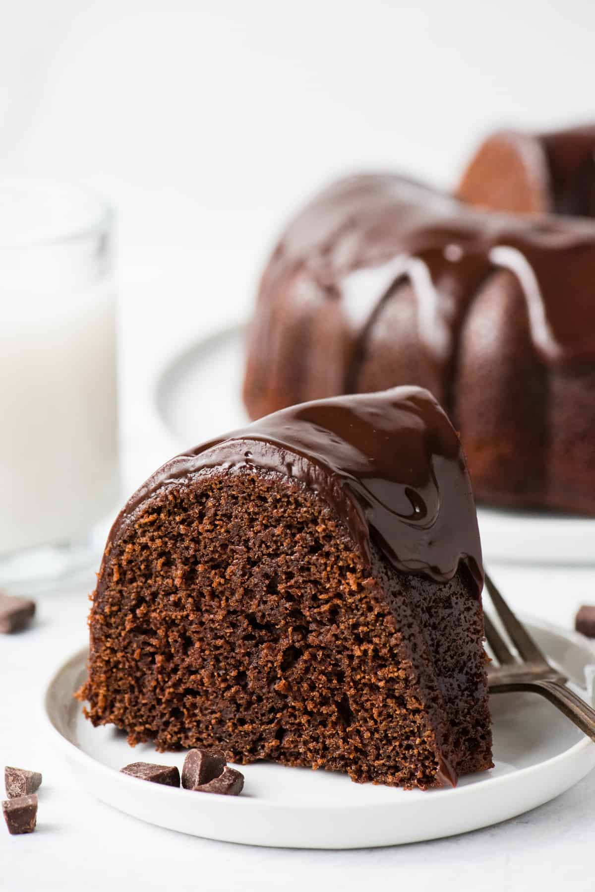 slice of chocolate bundt cake with chocolate glaze on white plate on white background