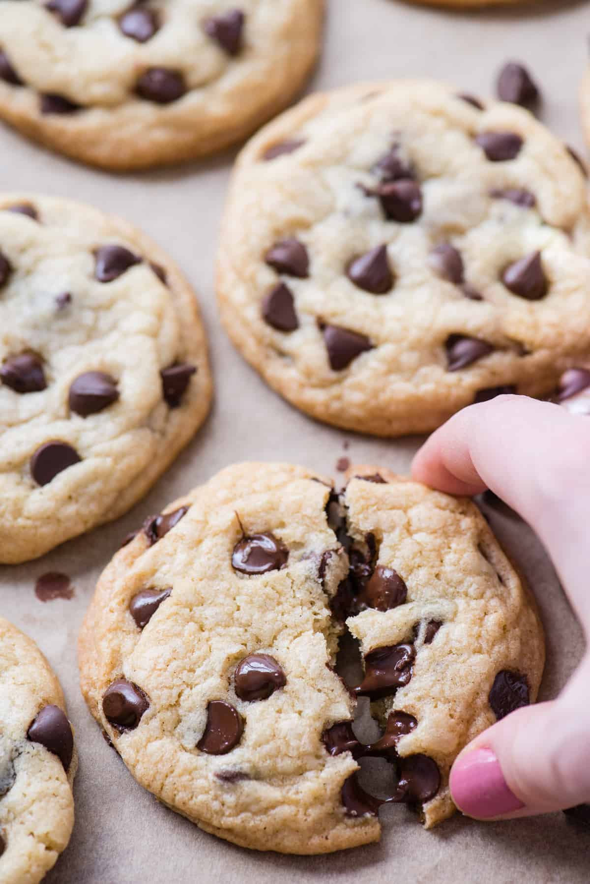hand grabbing half a chocolate chip cookie on brown parchment paper