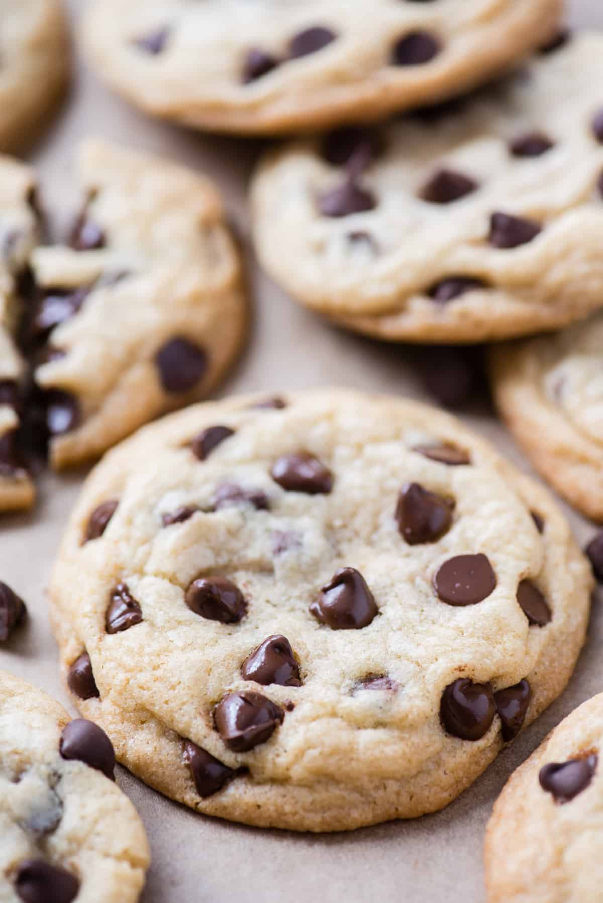 one chocolate chip cookie in focus on brown parchment paper with more cookies in the background