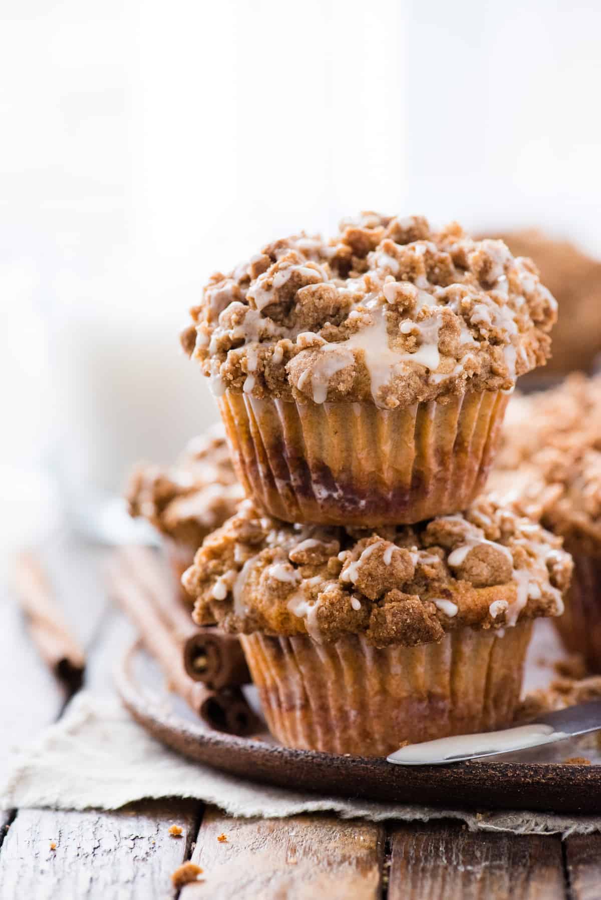 two coffee cake muffins with crumb topping stacked on top of each other on wood background