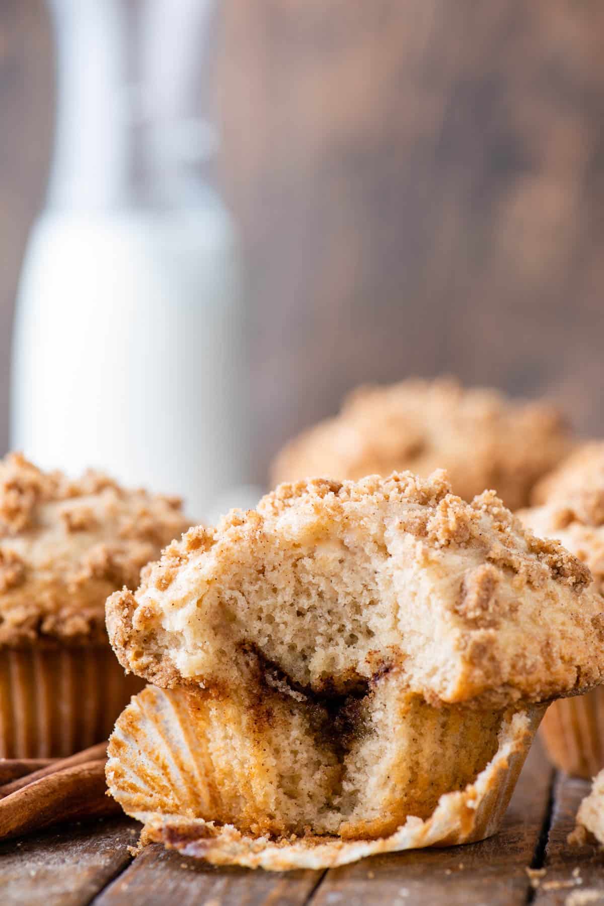 coffee cake muffins with bite removed showing cinnamon swirl layer inside on wood background