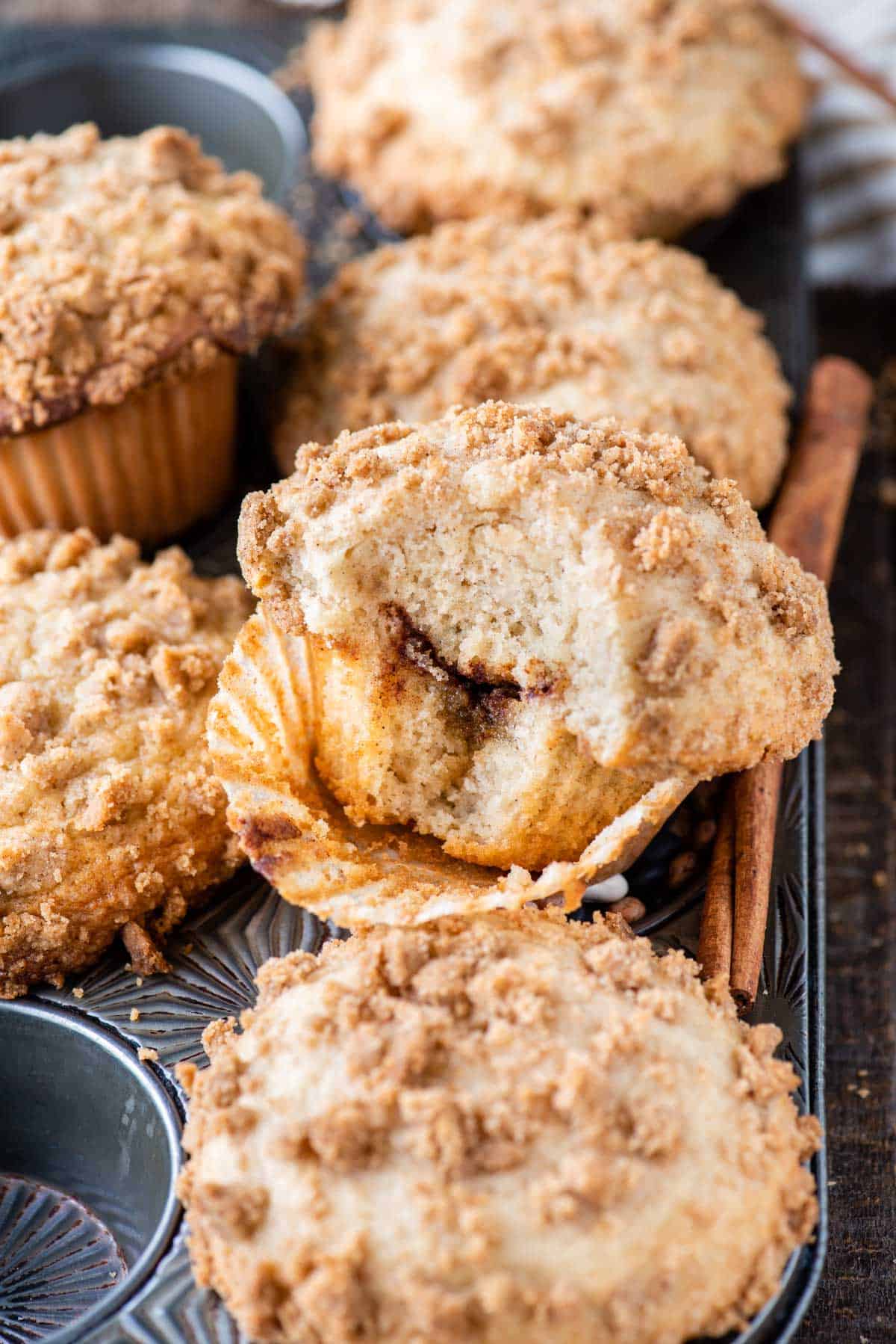 coffee cake muffins with bite removed showing cinnamon swirl layer inside on metal muffin pan