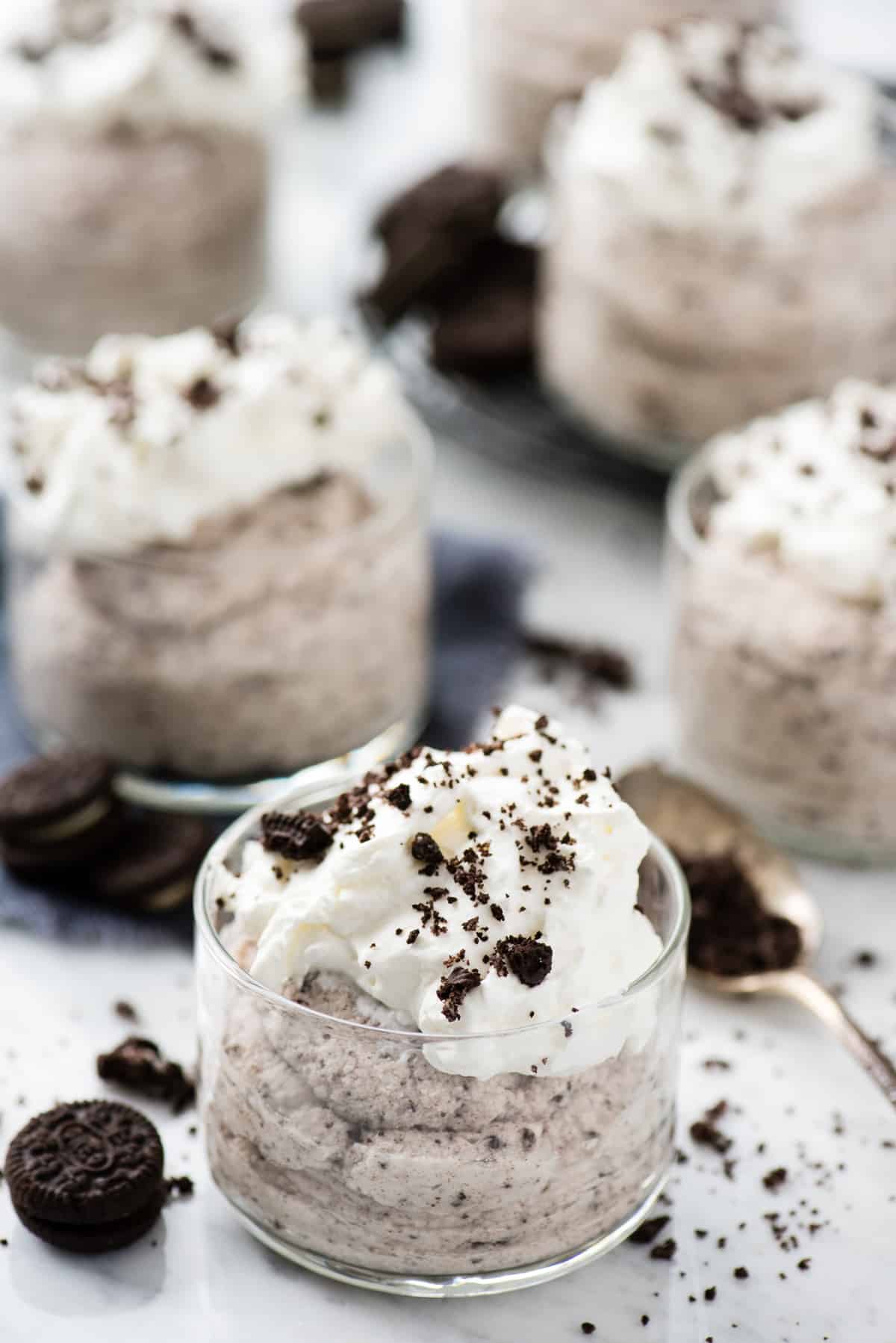 oreo mousse in glass dessert bowl topped with whipped cream and oreo pieces on white background