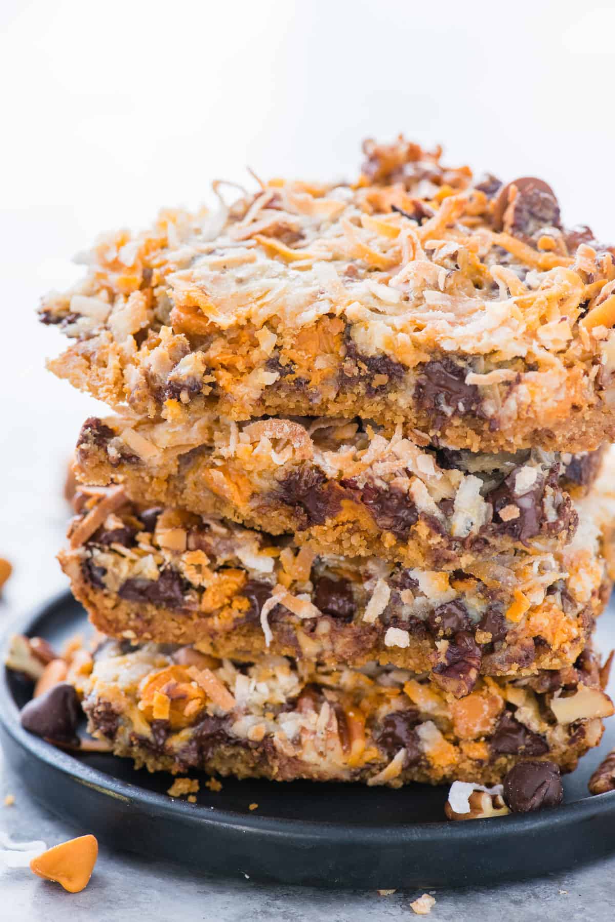 7 layer bars cut into squares stacked on top of each other on dark blue plate with white background