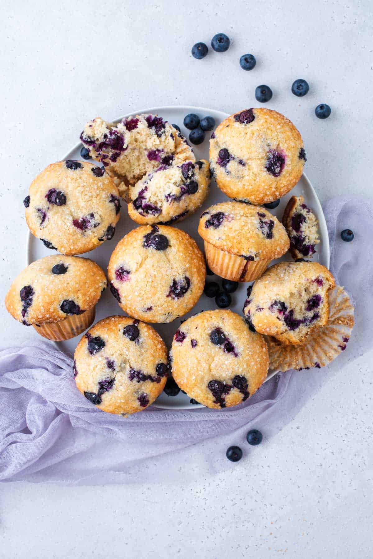blueberry muffins arranged on white tray with blueberries scattered around the tray