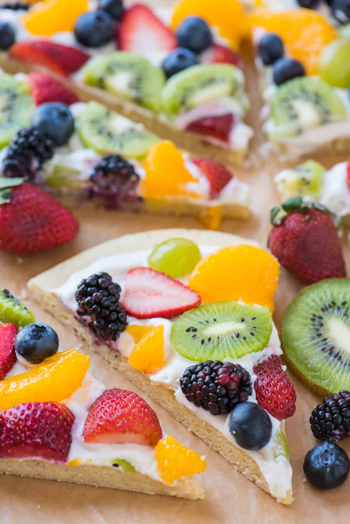 slice of fruit pizza strawberries, blueberries, mandarin oranges, kiwis and grapes on brown parchment paper