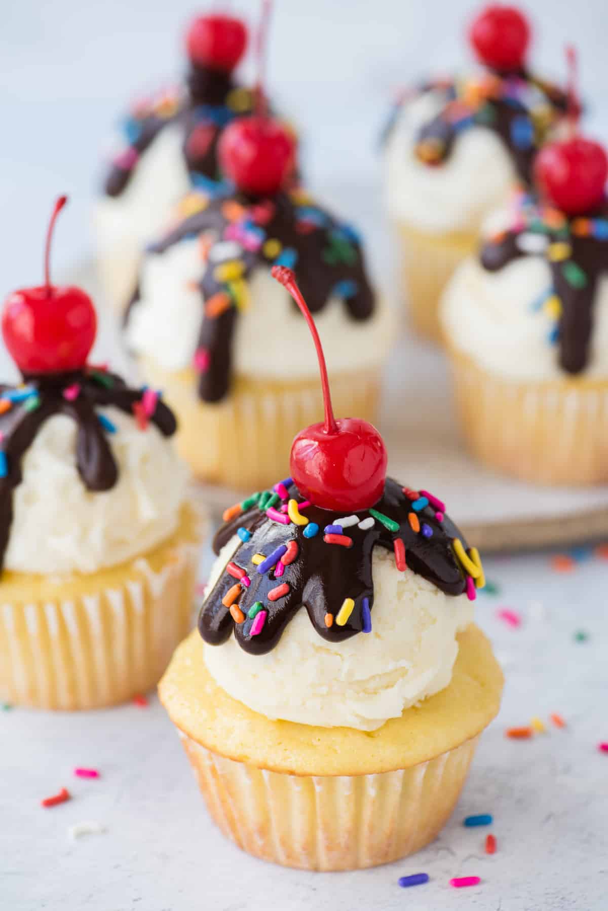 birthday cupcake with scoop of vanilla frosting, chocolate ganache drizzle, sprinkles and maraschino cherry on white background