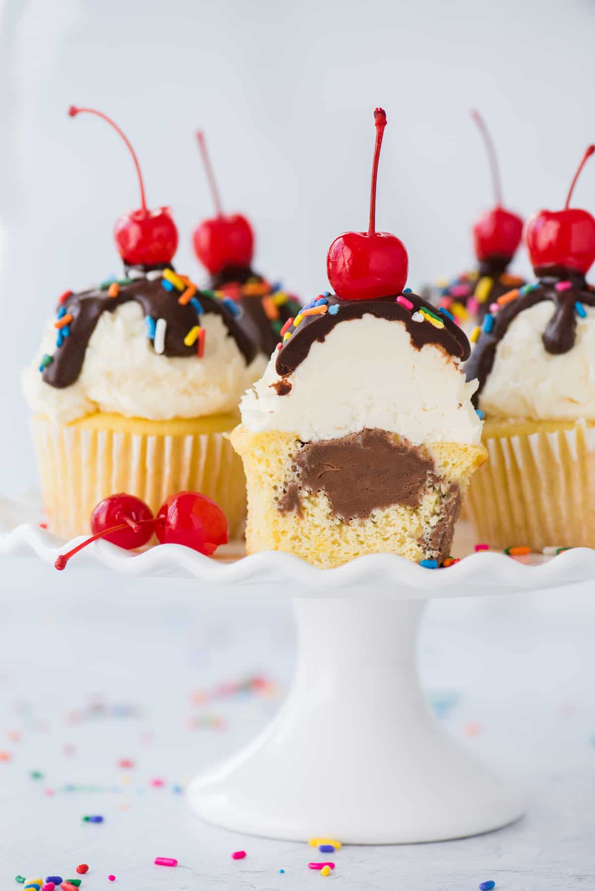 ice cream cupcakes with one cupcake cut in half showing chocolate ice cream center displayed on white cake stand on white background