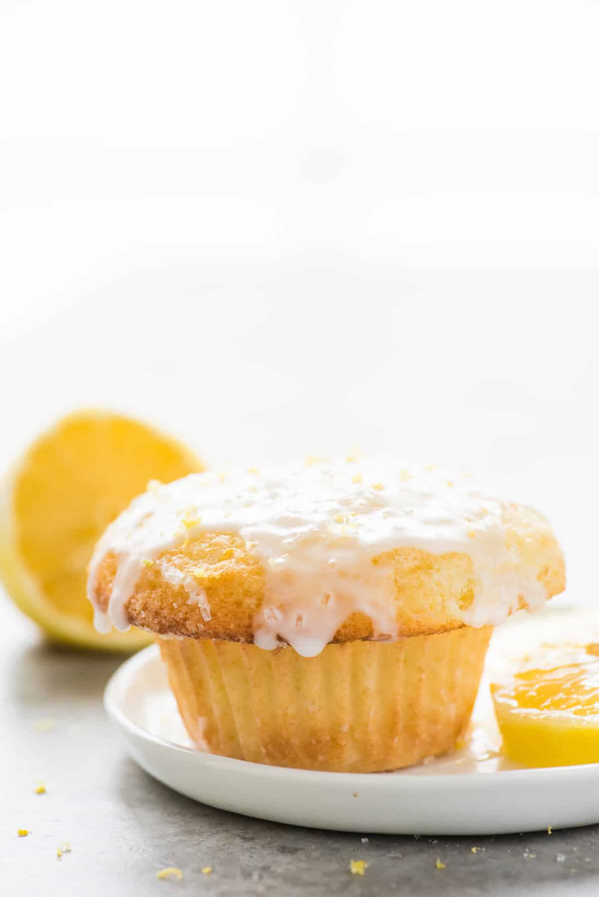 single lemon muffin with glaze on white plate on white background