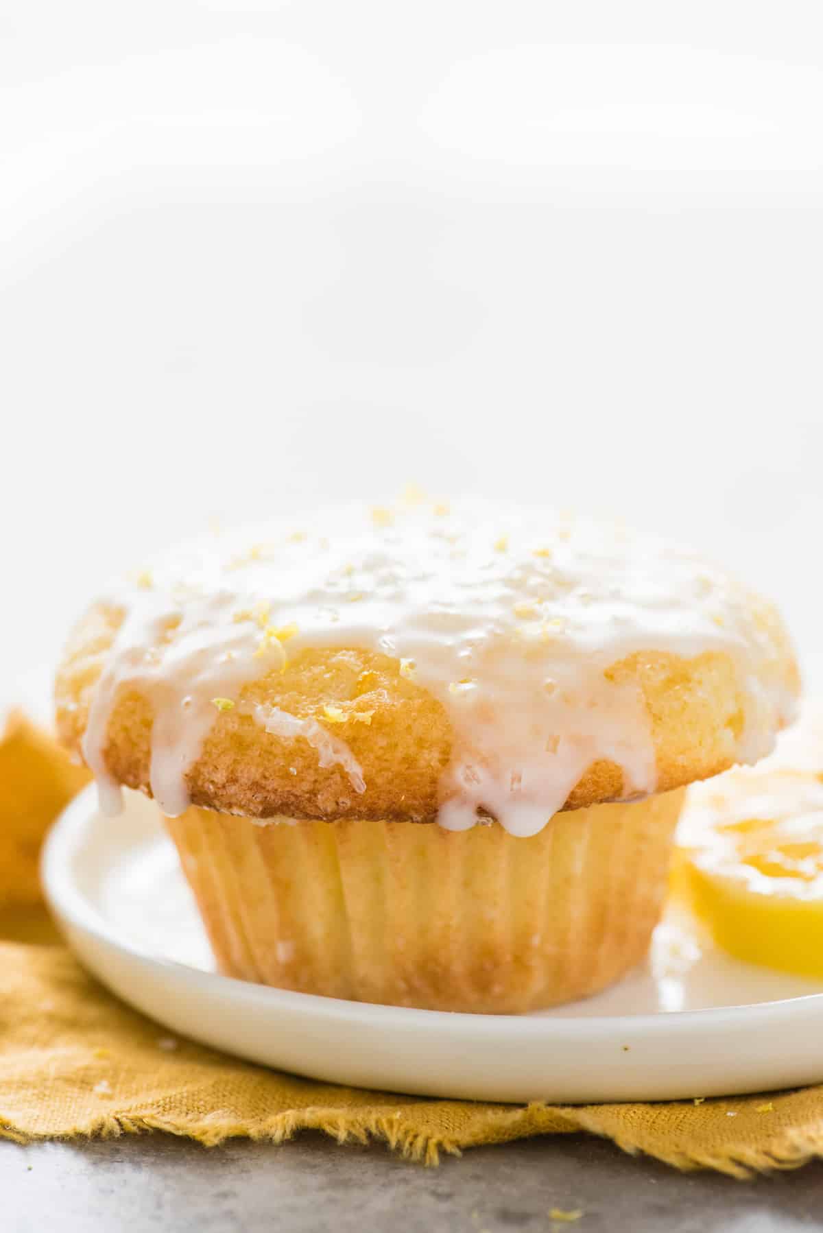 single lemon muffin with glaze on white plate on white background