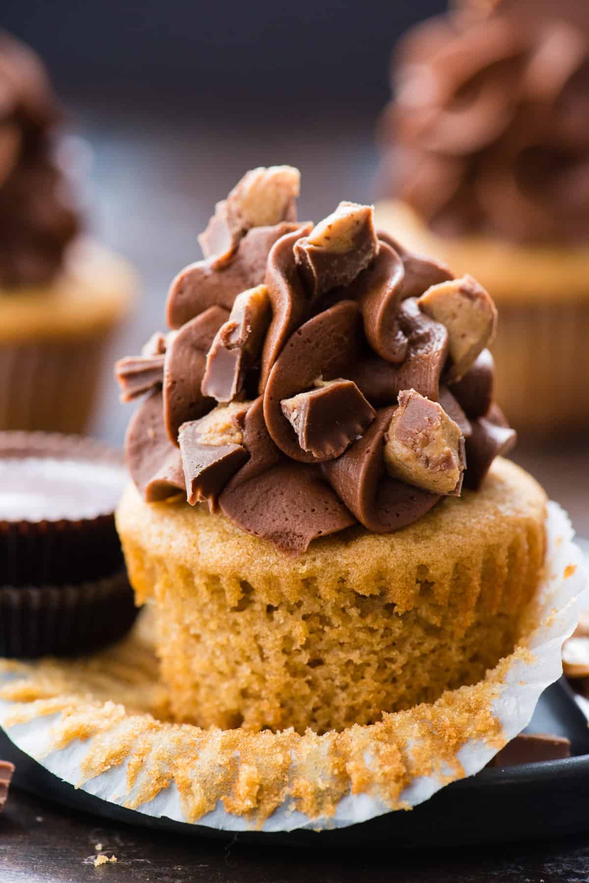 peanut butter cupcake with liner removed with chocolate frosting and reese’s crumbles